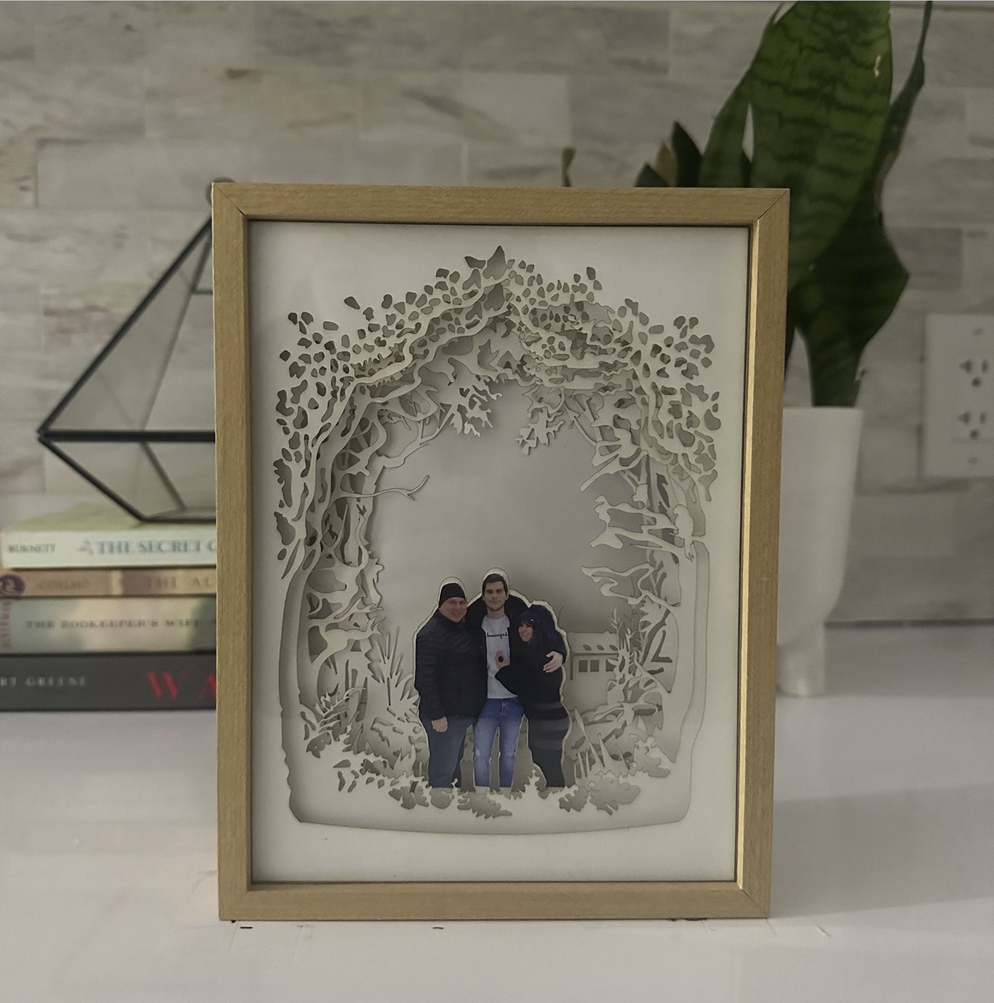 A custom family portrait lightbox. The centerpiece showcases a beautiful family portrait, while layers of carefully crafted cardstock create a lush and vibrant woodland setting. Ideal for unique home decor & personalized gifts.